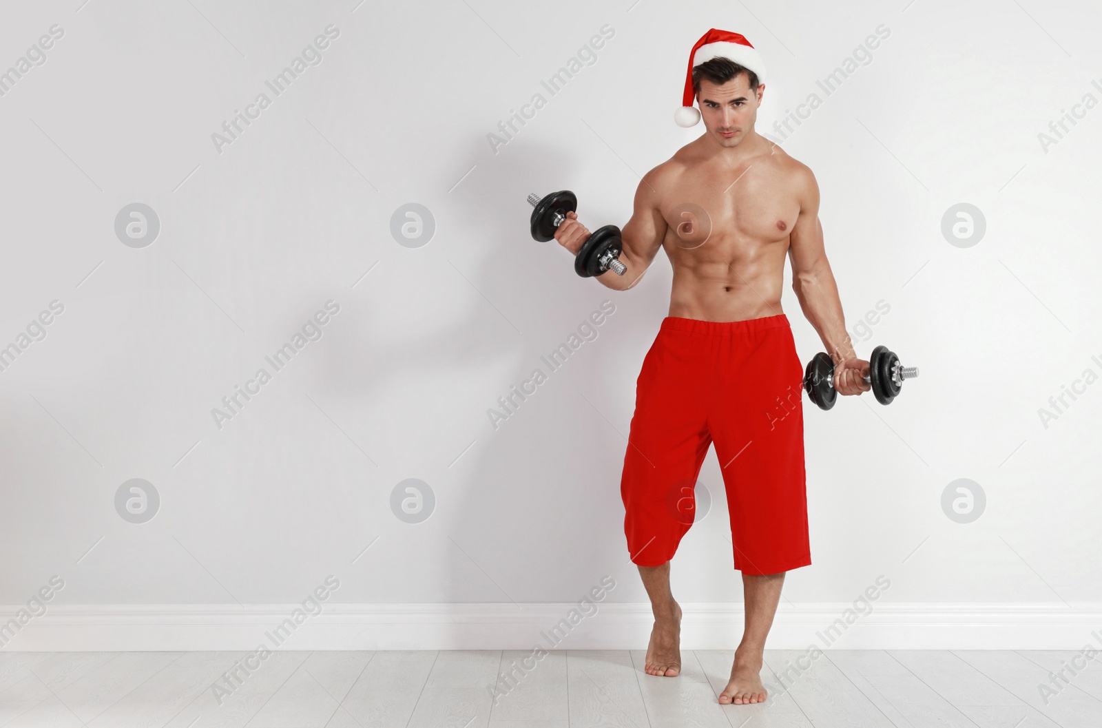 Photo of Sexy shirtless Santa Claus with dumbbells  near light wall, space for text