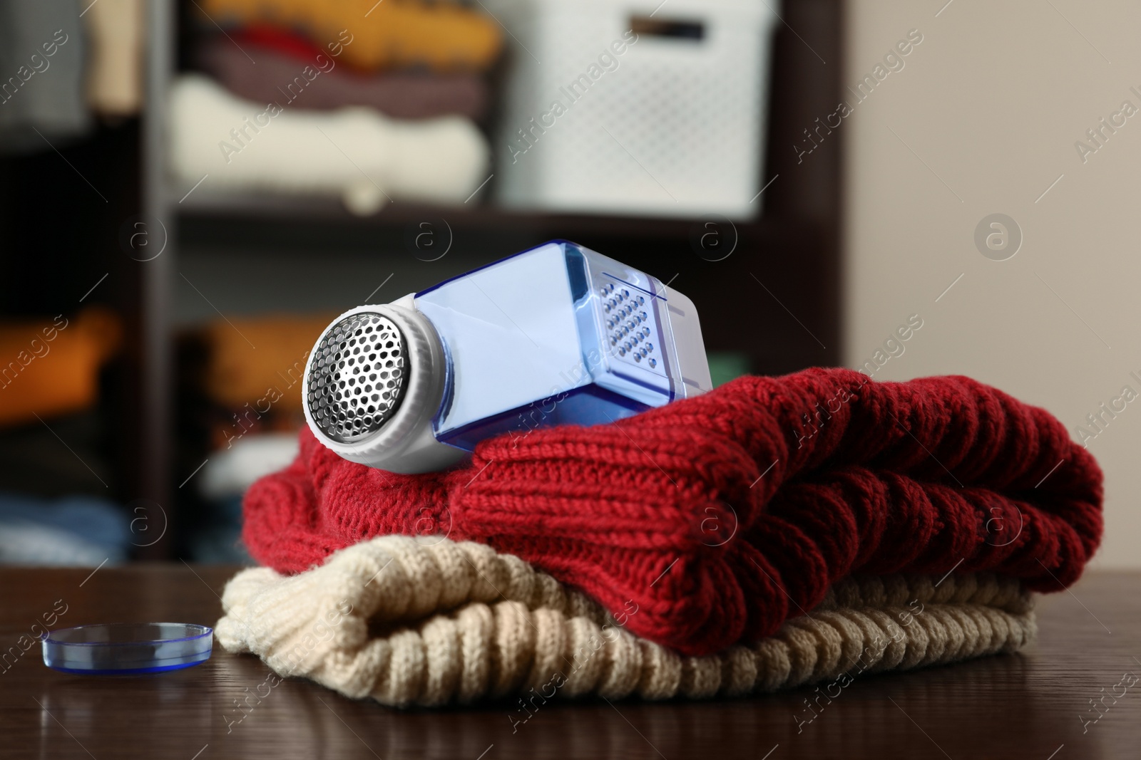 Photo of Modern fabric shaver and knitted clothes on wooden table indoors, closeup