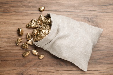 Photo of Overturned sack of gold nuggets on wooden table, flat lay