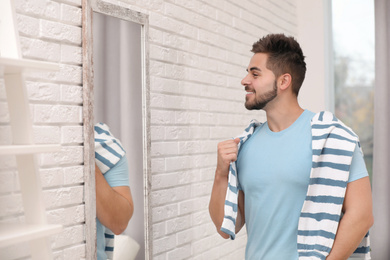 Young man looking at himself in large mirror at home