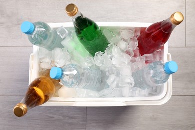 Photo of Plastic cool box filled ice cubes and refreshing drinks on wooden floor, top view