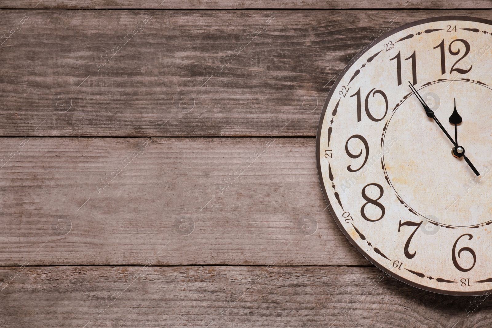 Photo of Clock showing five minutes until midnight on wooden table, top view with space for text. New Year countdown