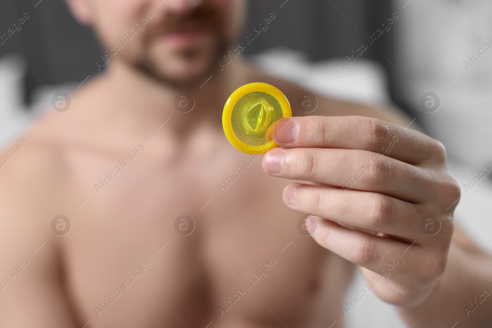 Photo of Closeup view of man showing condom on bed