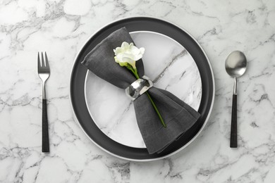 Photo of Stylish setting with cutlery, napkin, flowers and plates on white marble table, top view