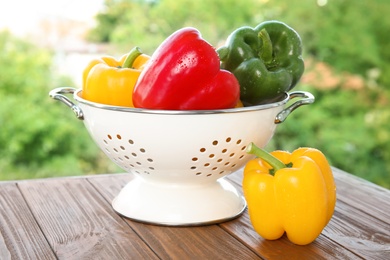 Photo of Colander with ripe paprika peppers on table against blurred background