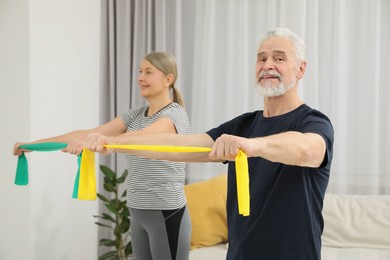 Photo of Senior couple doing exercise with fitness elastic bands at home, selective focus