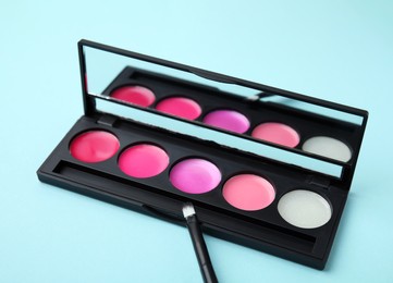 Photo of Cream lipstick palette and brush on light turquoise background, closeup. Professional cosmetic product