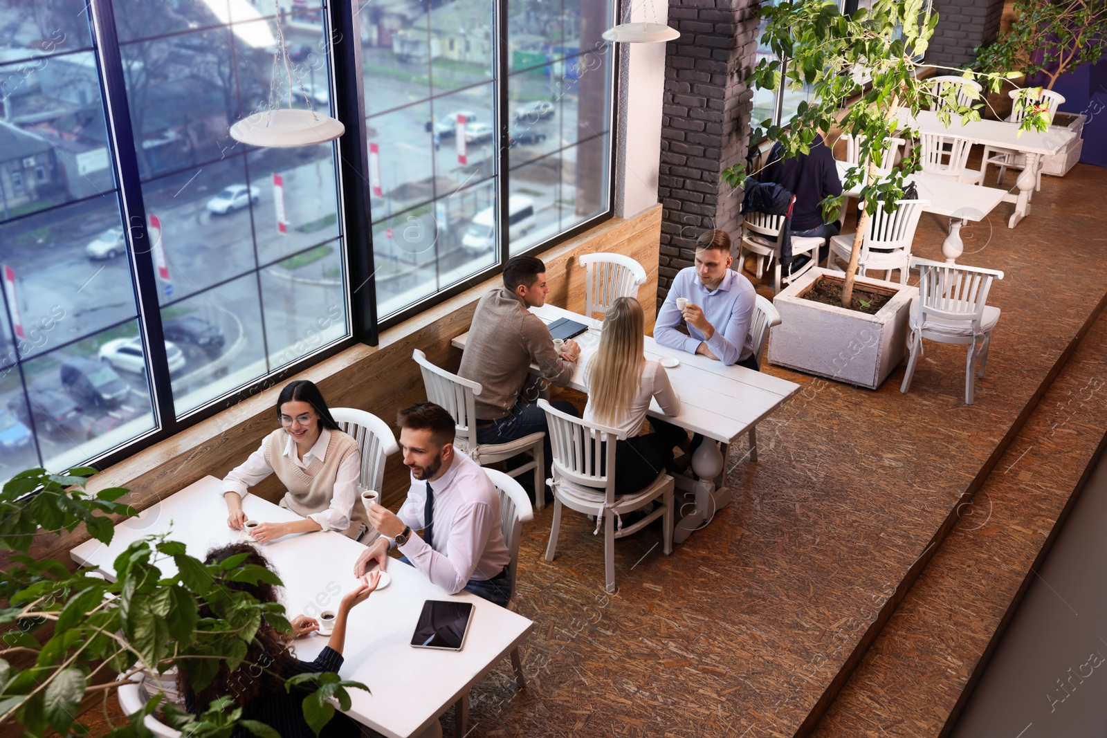 Photo of Coworkers having coffee break near window in cafe, above view