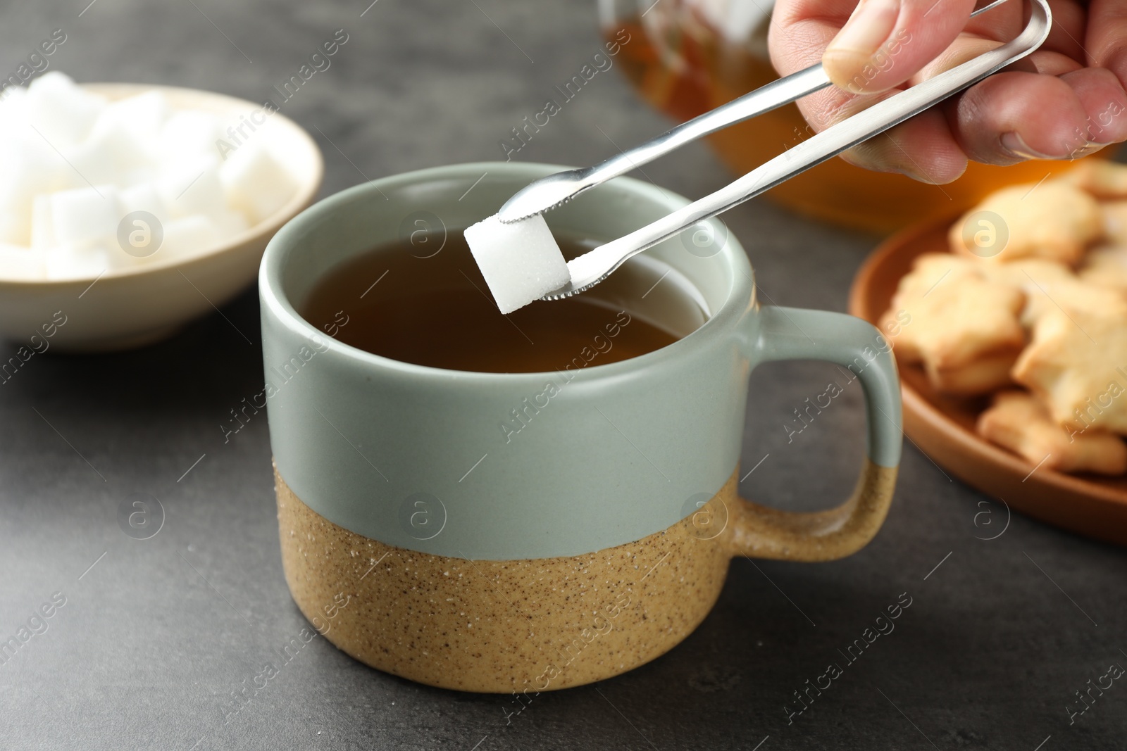Photo of Woman adding sugar cube into aromatic tea at grey table, closeup