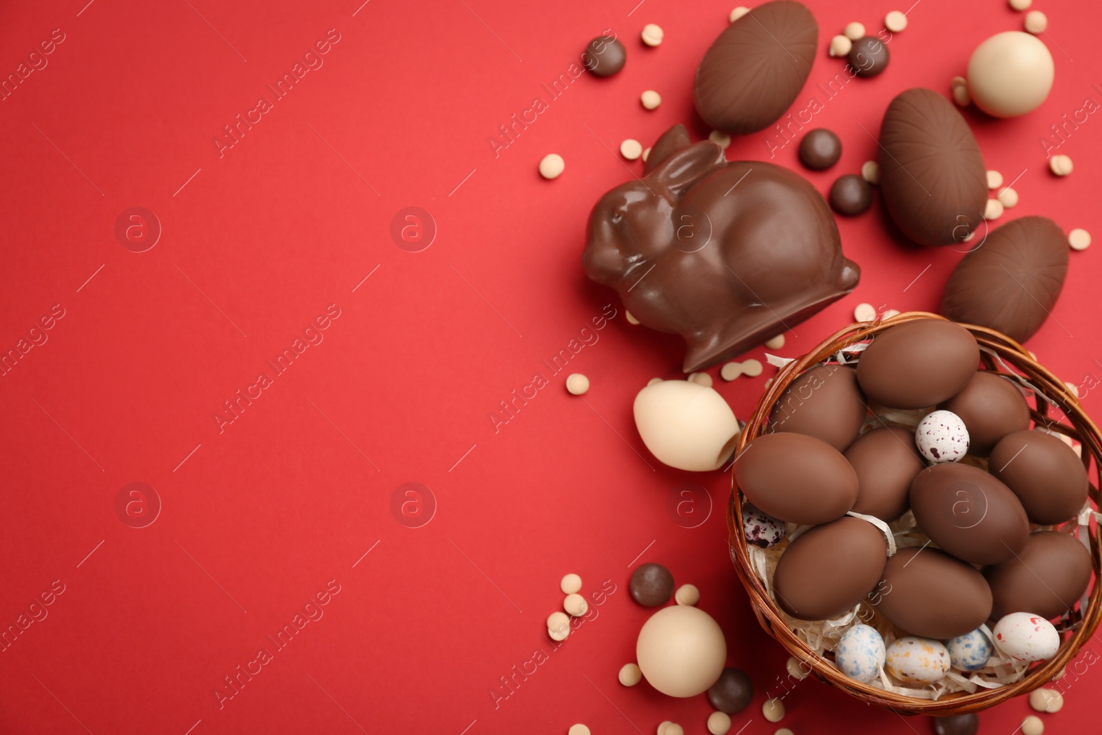 Photo of Flat lay composition with chocolate Easter bunny, eggs and candies on red background. Space for text