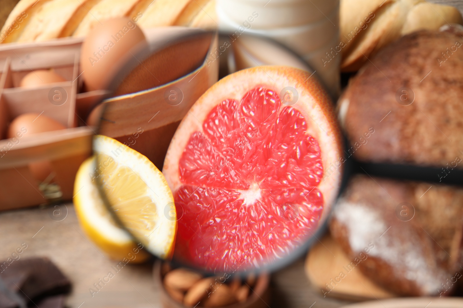Photo of Different products with magnifier focused on grapefruit and lemon, closeup. Food allergy concept