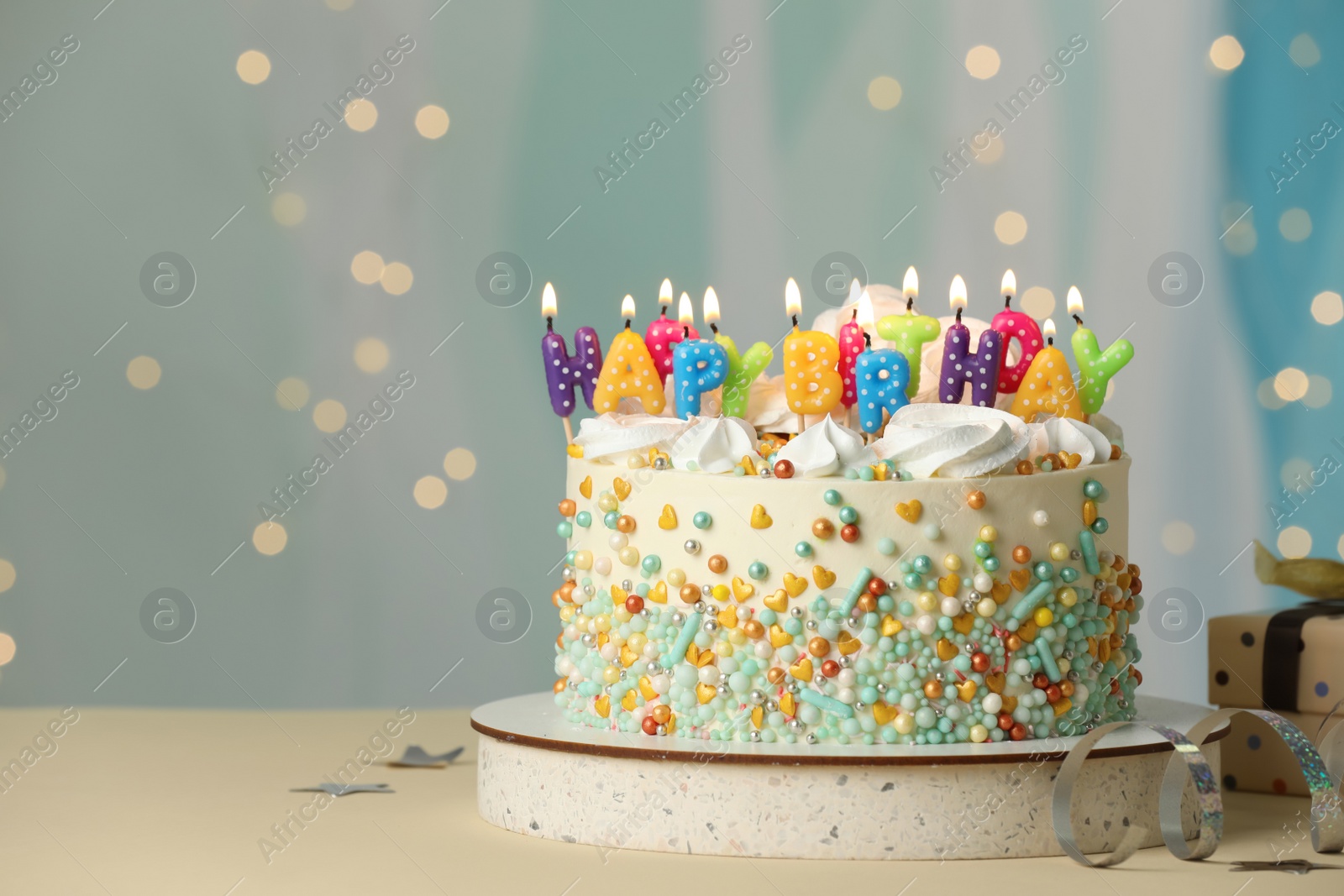 Photo of Beautiful birthday cake with burning candles and decor on white table. Space for text