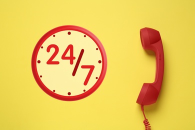 Image of 24/7 hotline service. Red handset on yellow background, top view