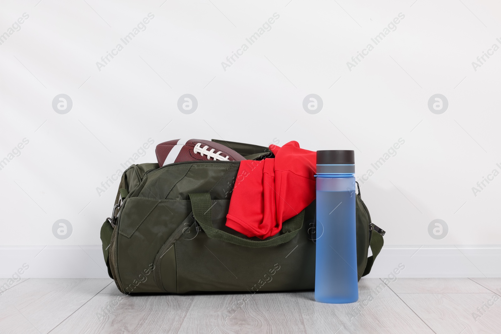 Photo of Gym bag and sports equipment on floor near white wall