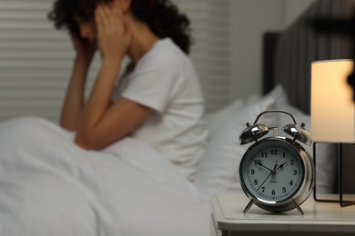 Photo of Woman suffering from headache in bed at night, focus on alarm clock