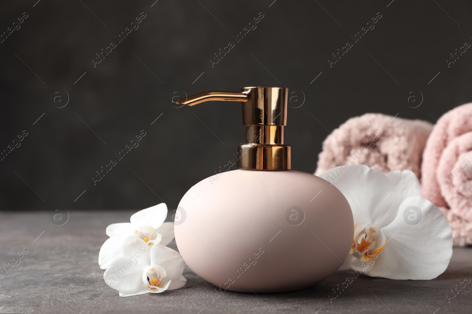 Photo of New stylish soap dispenser with flowers and towels on table