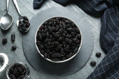 Bowl, spoon and jar of delicious ripe black mulberries on grey table, flat lay