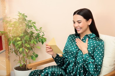 Photo of Happy woman reading greeting card on armchair in living room