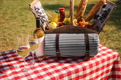 Photo of Picnic basket with wine, snacks and mat on table in park