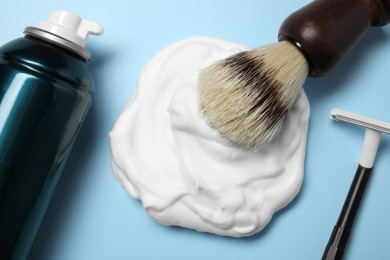 Photo of Bottle of shaving foam, brush and razor on light blue background, flat lay