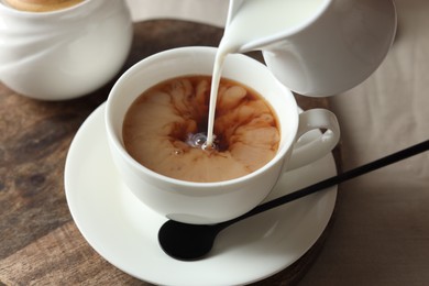 Photo of Pouring milk into cup with tea on light table, closeup