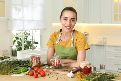 Young woman with vegetables and pickling jars at table in kitchen