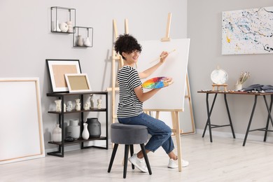 Young woman painting on easel with canvas in studio