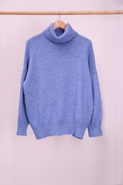 Stylish knitted sweater hanging on clothing rack near pink wall