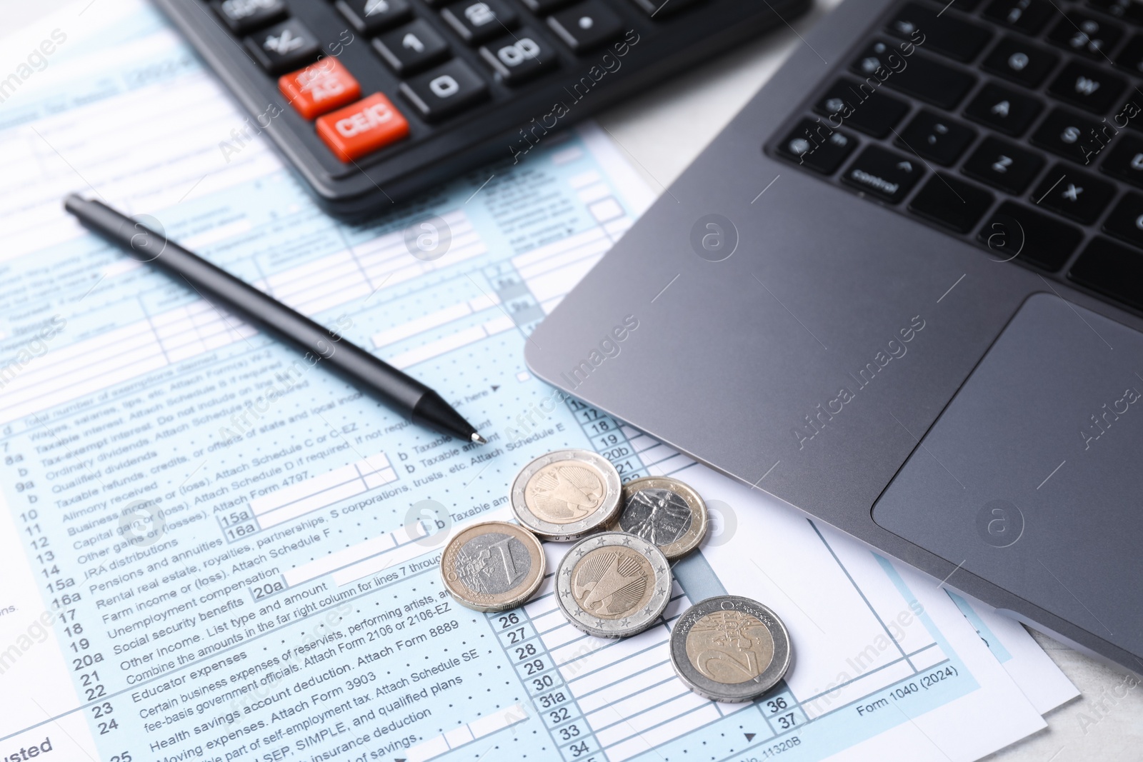 Photo of Tax forms, coins, pen, calculator and laptop on table, closeup
