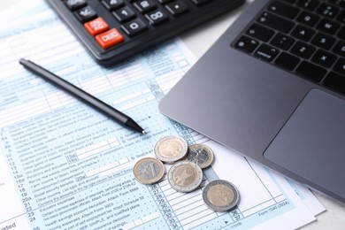 Tax forms, coins, pen, calculator and laptop on table, closeup