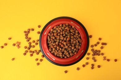 Dry dog food and feeding bowl on orange background, flat lay