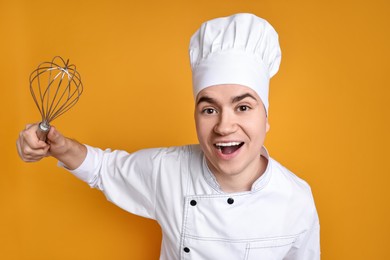 Photo of Portrait of happy confectioner in uniform holding whisk on orange background