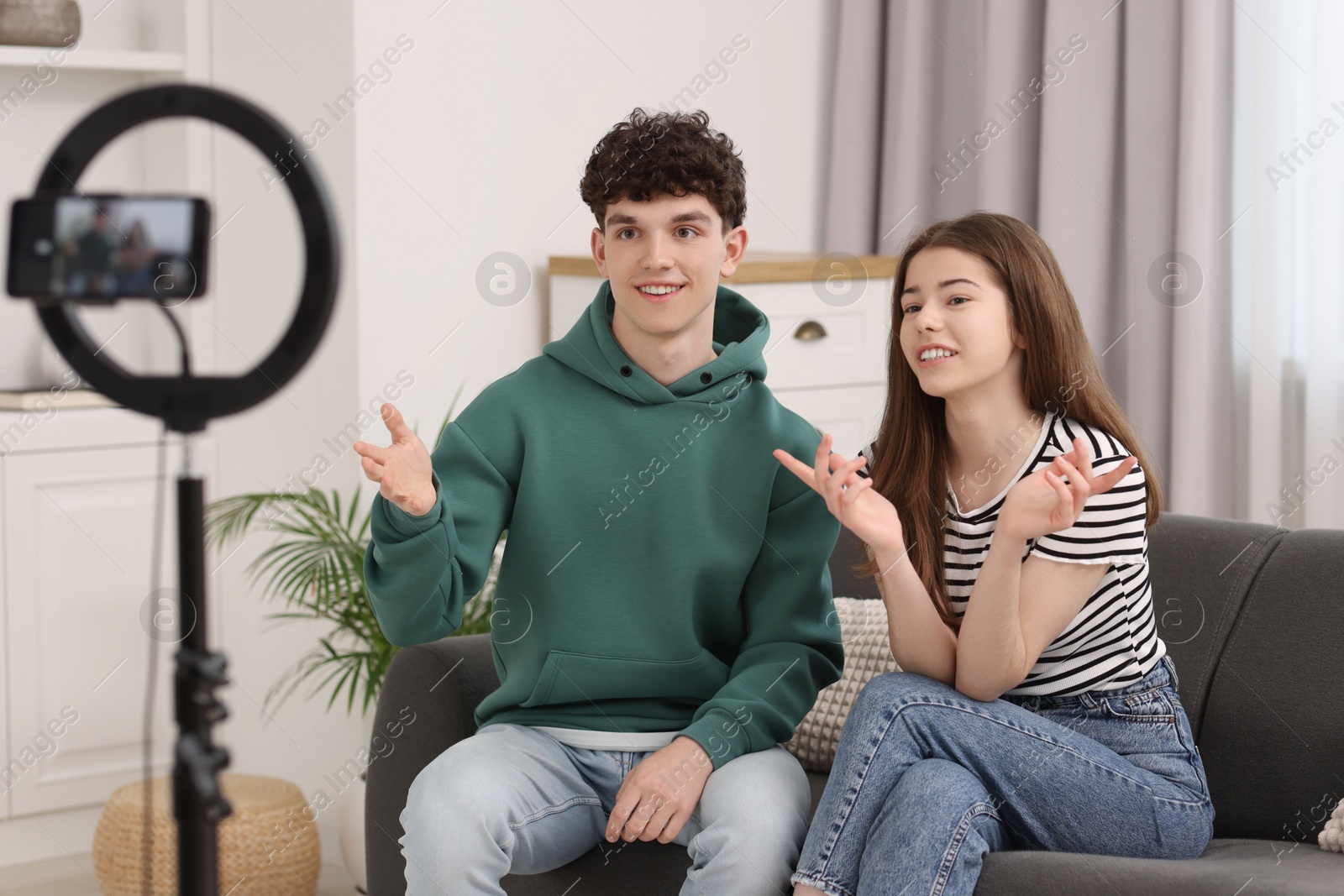 Photo of Smiling teenage bloggers talking while streaming at home