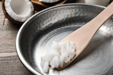 Photo of Frying pan with coconut oil and wooden spatula on wooden table, closeup. Healthy cooking