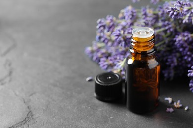 Bottle with essential oil near lavender on grey textured table, closeup. Space for text