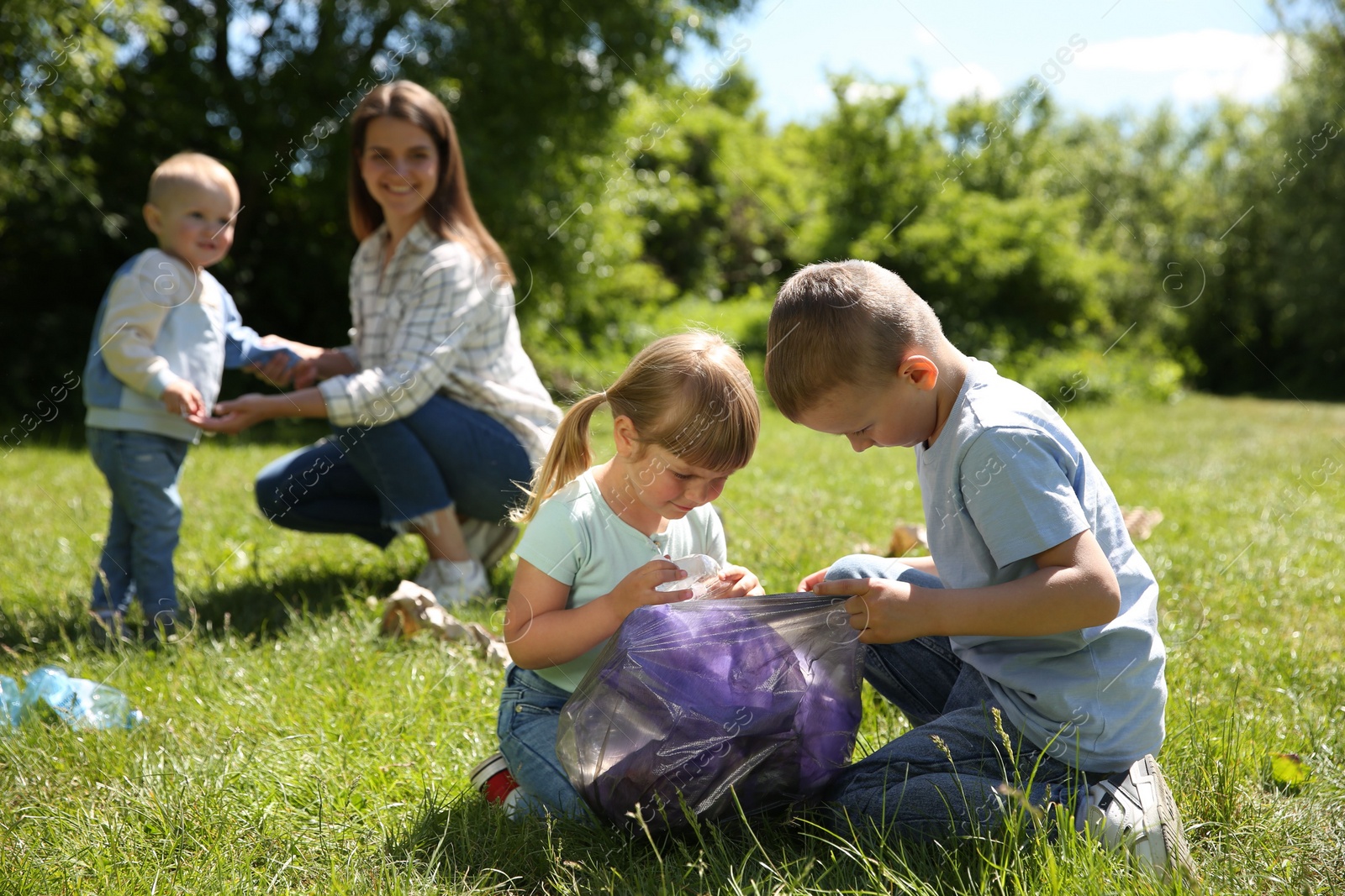 Photo of Mother and her children with plastic bags collecting garbage in park