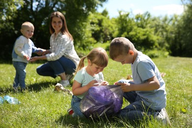 Mother and her children with plastic bags collecting garbage in park