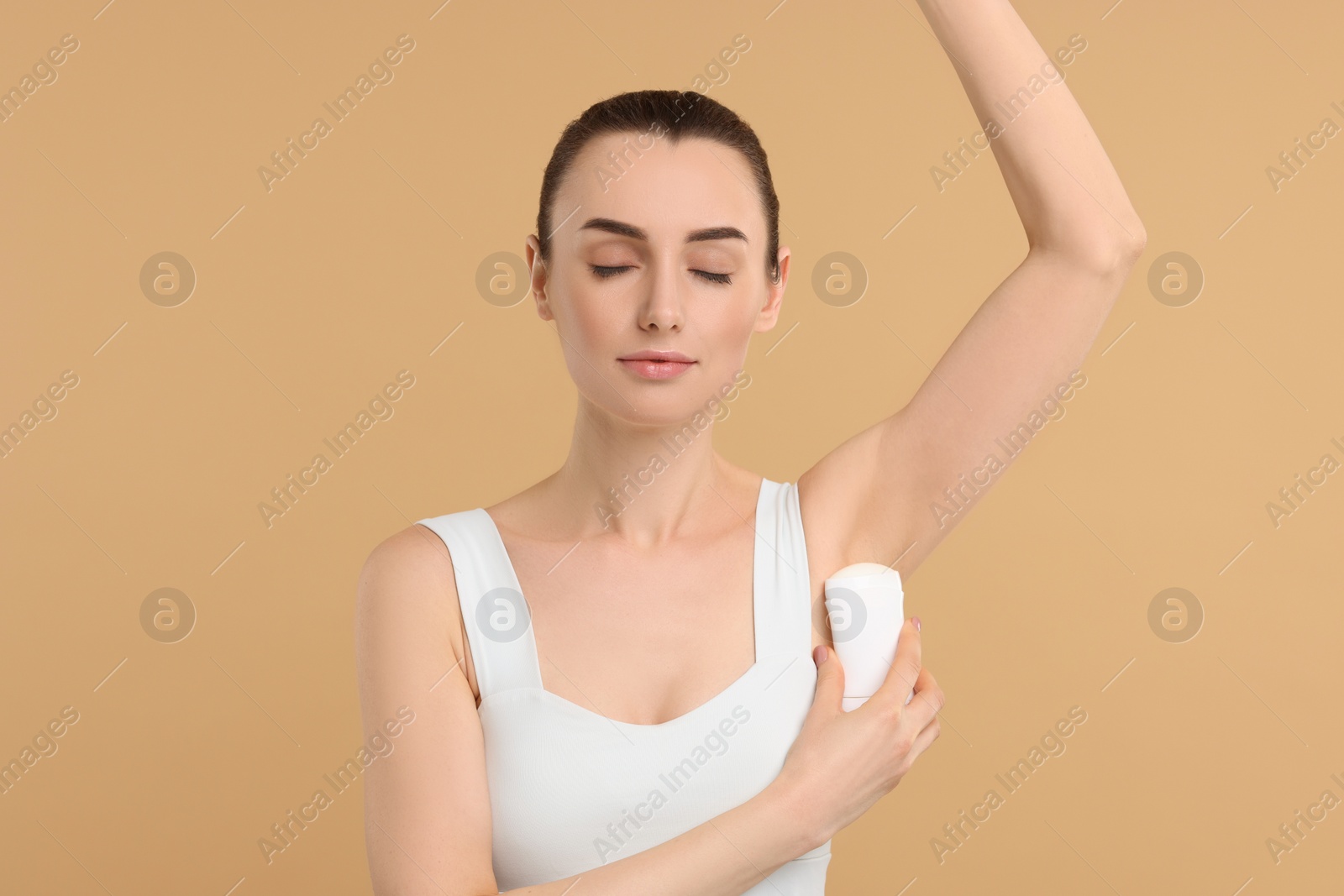 Photo of Beautiful woman applying deodorant on beige background