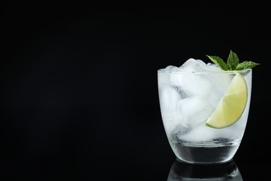 Glass of cocktail with vodka, ice and lime on black background. Space for text