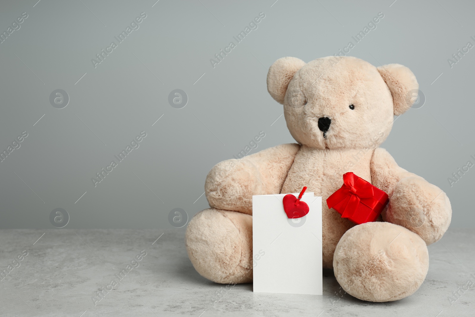 Photo of Cute teddy bear with gift box and blank card on light grey table, space for text. Valentine's day celebration