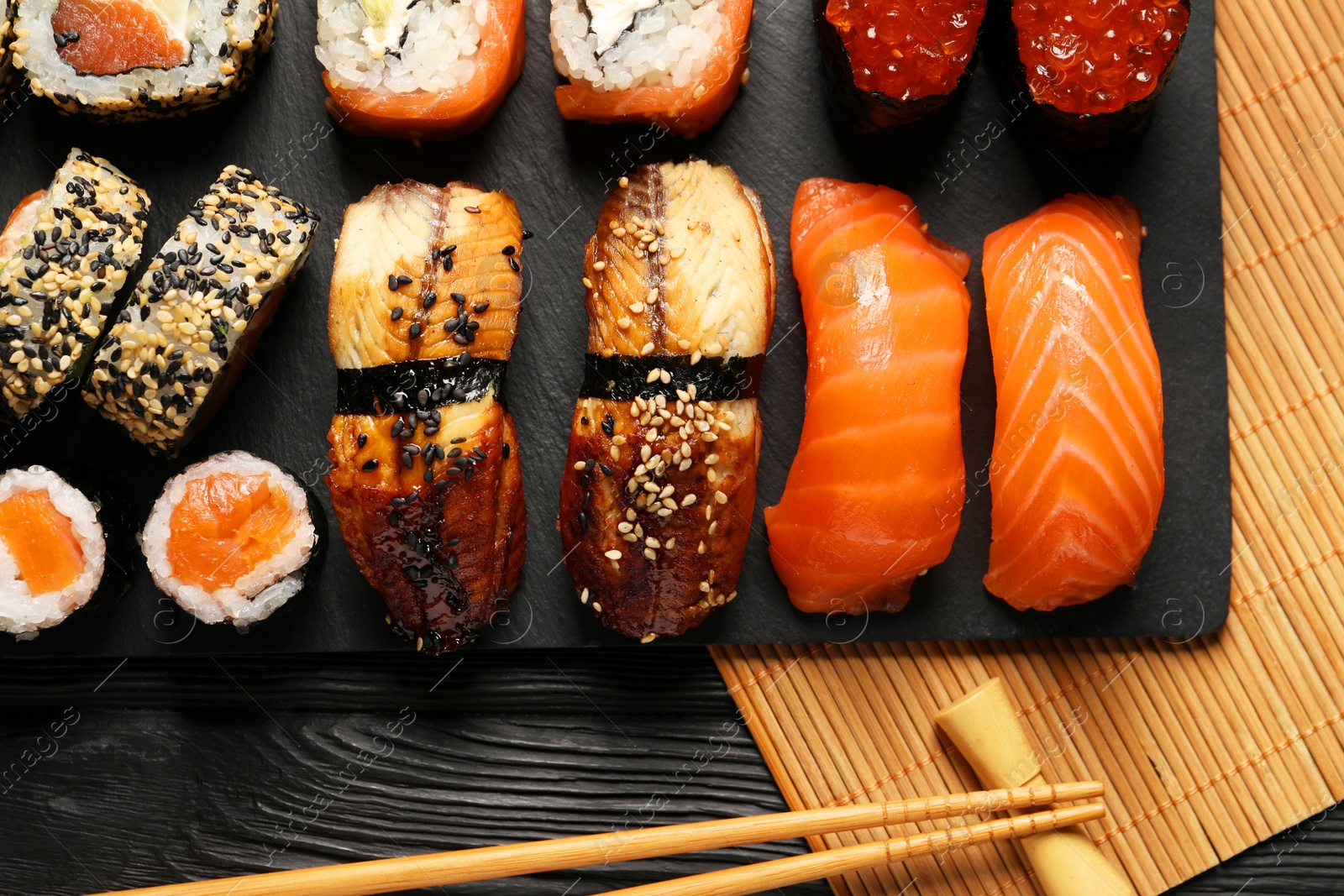 Photo of Delicious sushi rolls and chopsticks on black wooden table, flat lay