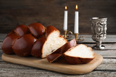 Photo of Cut homemade braided bread, goblet and candles on wooden table. Traditional Shabbat challah