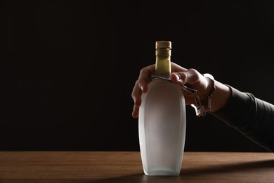 Photo of Alcohol addiction. Man handcuffed to bottle of vodka at wooden table, closeup. Space for text