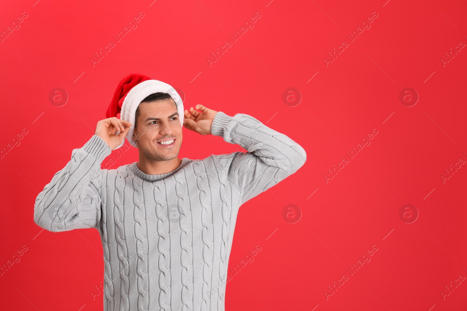 Photo of Handsome man wearing Santa hat on red background, space for text