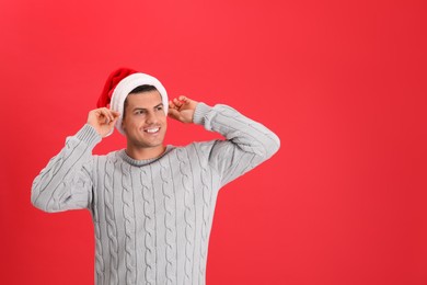 Handsome man wearing Santa hat on red background, space for text