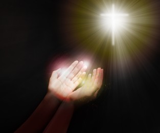 Image of Woman stretching hands towards cross silhouette in darkness, closeup. Praying concept