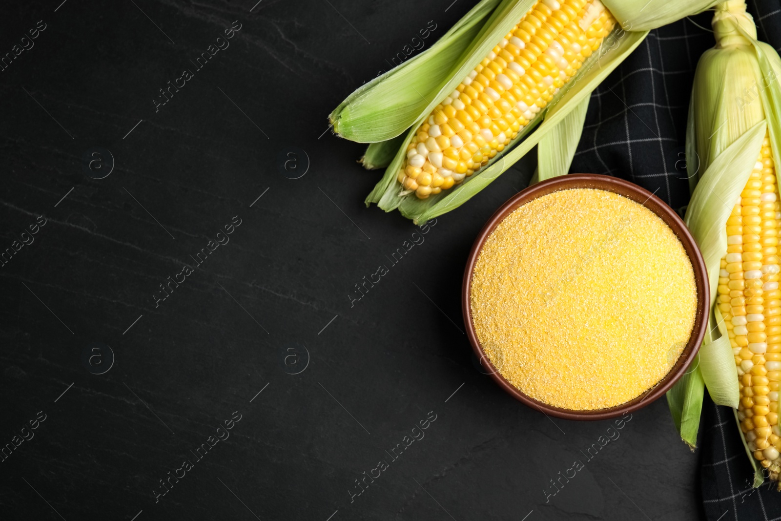 Photo of Cornmeal in bowl and fresh cobs on black table, flat lay