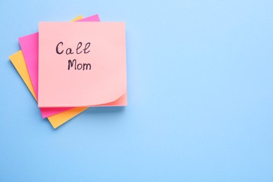 Paper note with phrase Call mom on light blue background, top view. Space for text