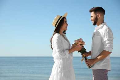 Photo of Young man giving flowers to his wife at beach. Honeymoon trip