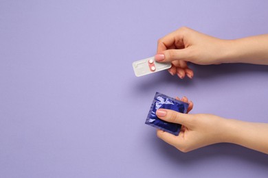 Photo of Woman holding condom and contraceptive pills on violet background, top view with space for text. Choosing birth control method